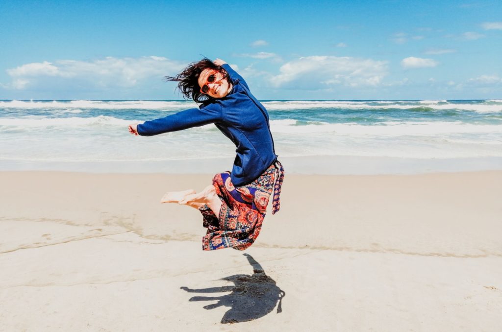 a man jumping in the air on a beach with a toy car