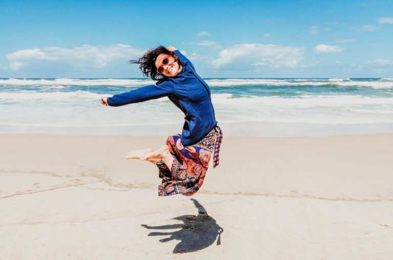 a man jumping in the air on a beach with a toy car