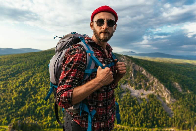 a man wearing a red hat and sunglasses standing on a hill with a valley and hills in the